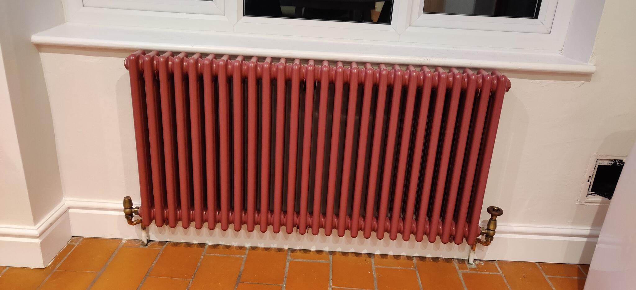 Red column radiator fitted under a window with brass valves