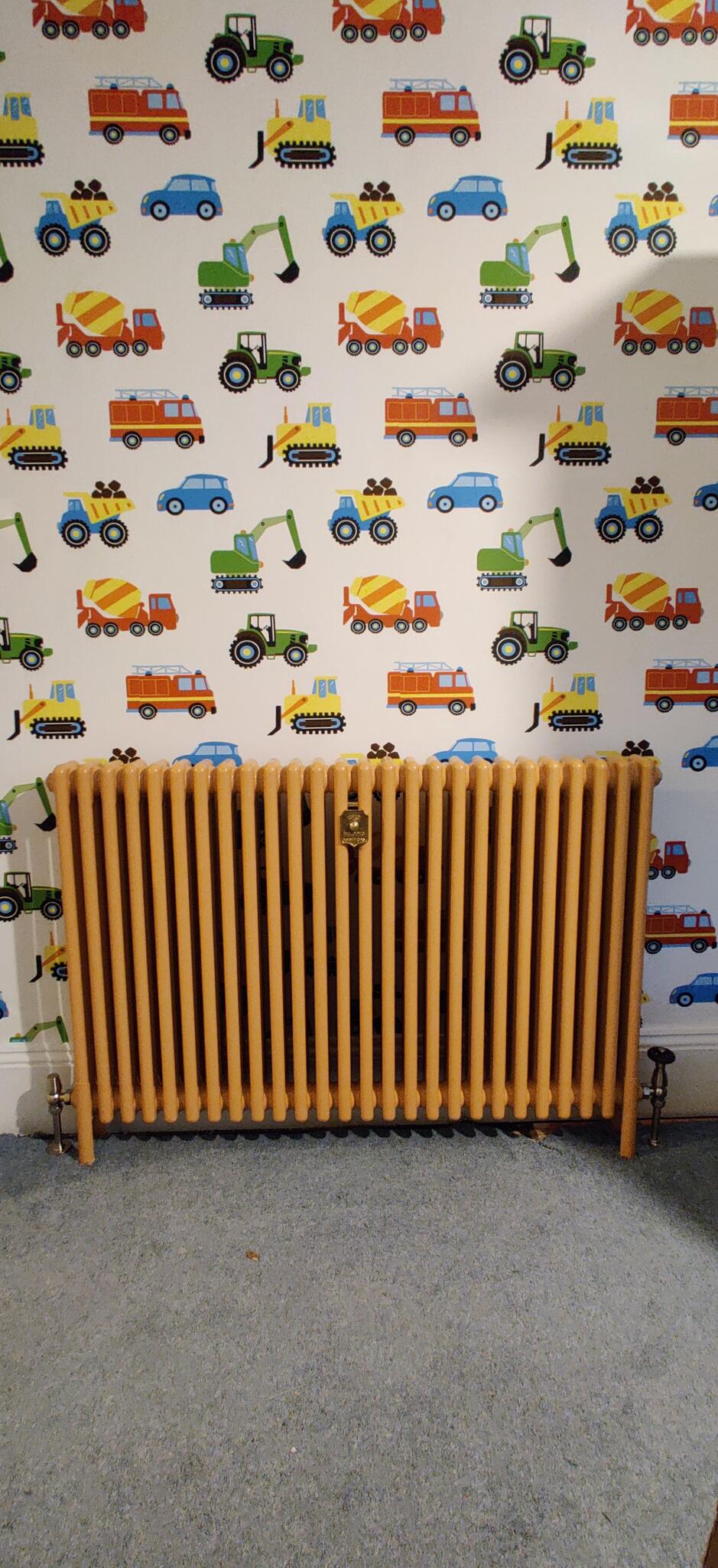 Yellow column radiator fitted in a room with vehicle-pattern wallpaper
